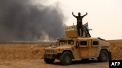 A member of Iraqi government forces flashes the sign for victory as he stands on a military vehicle while smoke billows from oil wells set ablaze by Islamic State militants before they fled the region of Qayyarah late last month.