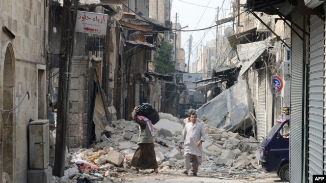 Syria -- Civilians walk past debris from destroyed buildings in the old sector of the northern city of Aleppo, 23Oct2012