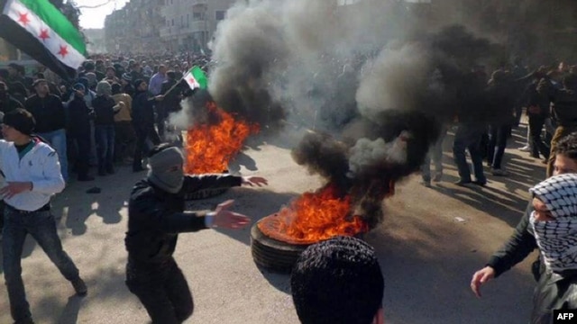 A handout picture released by Local Coordination Committees in Syria shows protesters burning tires and waving independence flags during an antigovernment demonstration in a Damascus suburb on February 4.