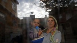 A Syrian refugee woman holds her son as she stands at the window of their friend's house at the Syrian-Turkish border town of Ceylanpinar in Syria.