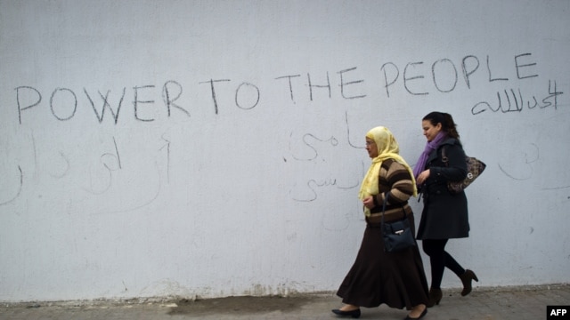 Two women walk past a wall surrounding the burnt and looted house that belonged to the nephew of ousted president in the Tunisdan town of Hammamet.