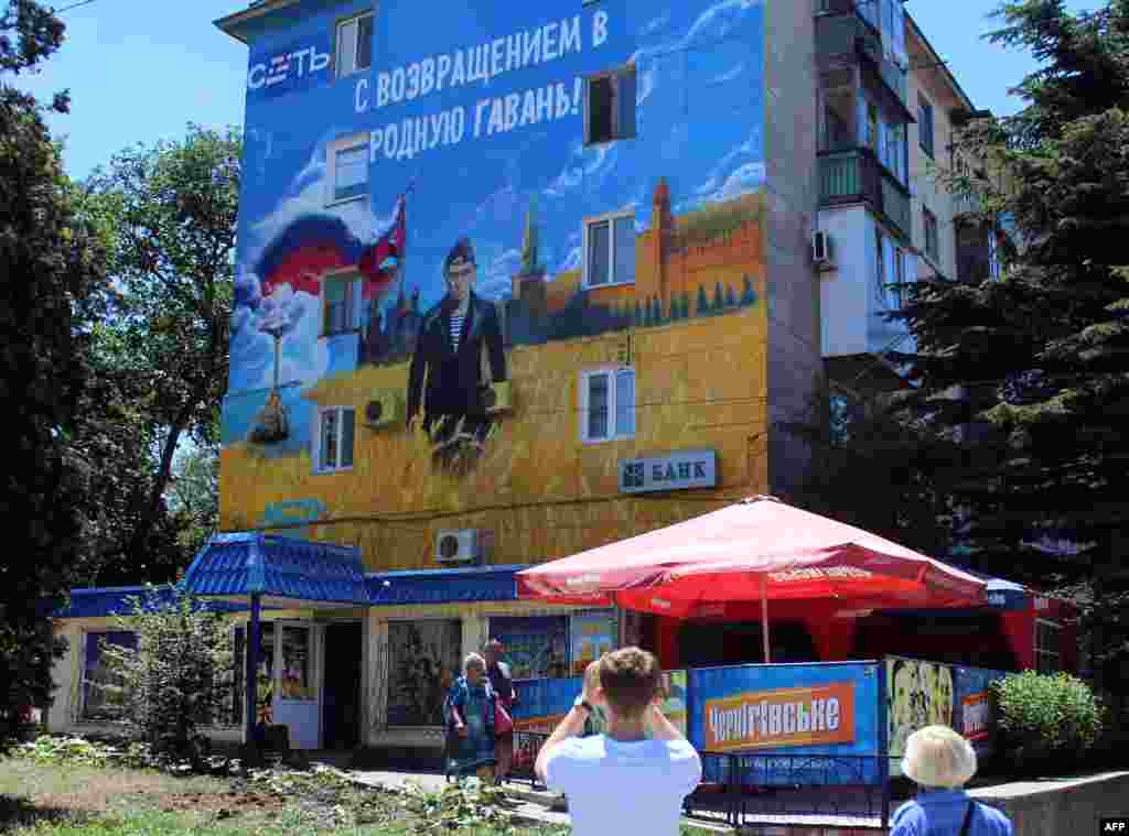 Pedestrians walk by a mural depicting Russian President Vladimir Putin dressed as a Russian Navy seaman, in the Crimean city of Sevastopol. (AFP Yury Lashov)