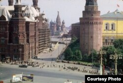 An entrance to Moscow's Red Square, with St. Basil's Cathedral in the distance, and the State Historical Museum to the left. Thousands of people can be seen standing in a long, snaking line to enter Lenin's mausoleum.