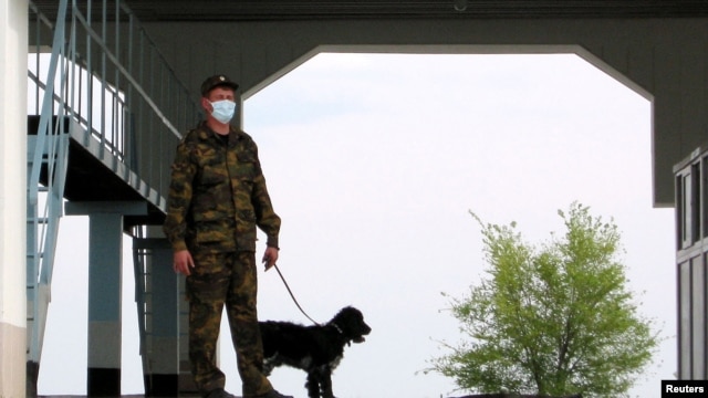 A masked border guard with a canine stands at an empty vehicle checkpoint at the Korgas crossing point, the largest on the 1,500-kilometer Kazakh-Chinese border in May.