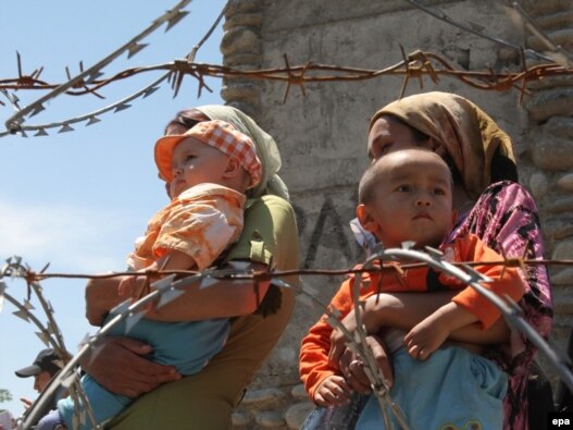 Ethnic Uzbek refugees walk behind a barbed wire fence as they queue to return to Kyrgyzstan at the border crossing near the city of Osh