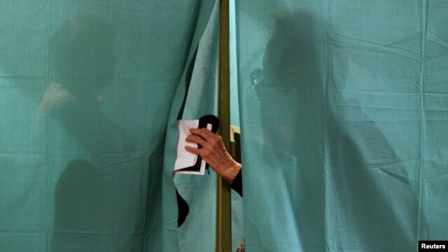 People are seen behind the curtain of a voting booth in Minsk during parliamentary elections on September 23.
