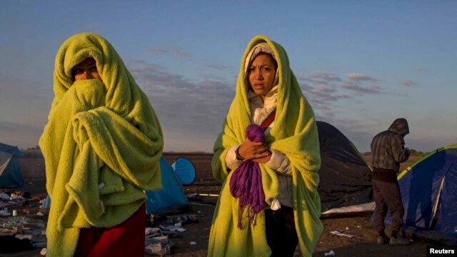 Hungary -- Migrants wrap themselves in blankets to warm up as the sun rises at a collection point in the village of Roszke, September 9, 2015