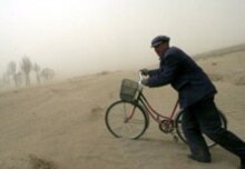 China – Environment / deforestation – Villager pushes his bike through a sandstorm, Xinglong village, Kangbao region, Hebei Province, 21 April 2006. (Size: 220x155.) Source: epa.