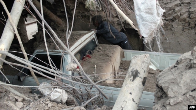 A man inspects a destroyed car trapped under the rubble of a house in the eastern village of Shaj.