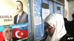 A woman stands near election posters for current Azerbaijani President Ilham Aliyev