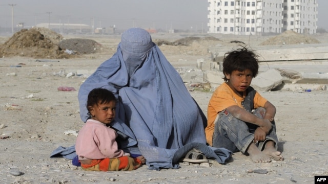 A burqa-clad woman begs with her children near a newly constructed building in Kabul.