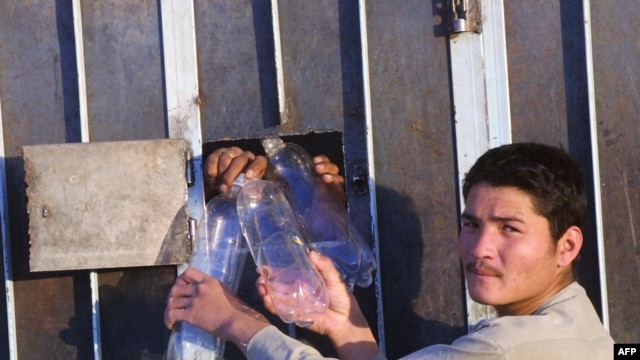 An Afghan man takes empty water bottles from Afghan men in Iranian detention in the southeastern Iranian city of Zahedan (file photo). Afghan officials say more than 5,600 Afghan nationals are in Iranian prisons for alleged drug crimes.