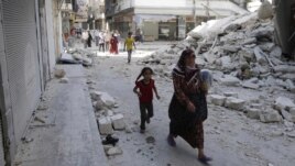 Syria -- Civilians walk near a destroyed building after a Syrian Air Force fighter jet launched a bomb in the city of Aleppo, 03Sep2012