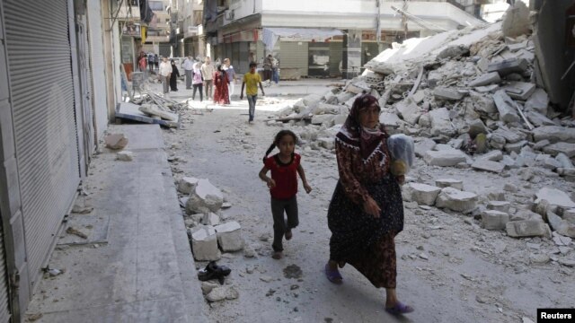 Syria -- Civilians walk near a destroyed building after a Syrian Air Force fighter jet launched a bomb in the city of Aleppo, 03Sep2012