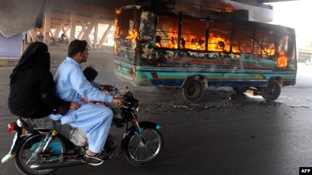 A Pakistani family rides past a burning bus during a week of violence in the restive city of Karachi. 