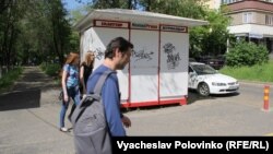 Люди идут на фоне закрытого газетного киоска в Алматы.