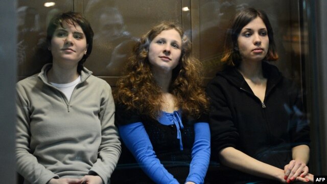 Pussy Riot members Maria Alyokhina (left to right), Yekaterina Samutsevich, and Nadezhda Tolokonnikova sit in a glass-walled cage in a courtroom in Moscow in October 2012 during their trial.