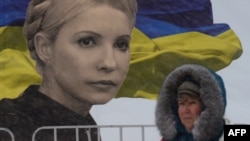 A woman walks in front of a giant poster bearing a picture of jailed Yulia Tymoshenko and a Ukrainian flag on Independence Square in Kyiv
