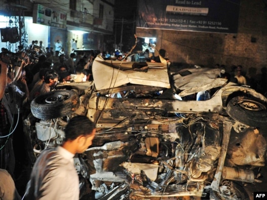 People gather around the destroyed car after the bomb explosion in Peshawar, which killed Nasrullah Afridi.