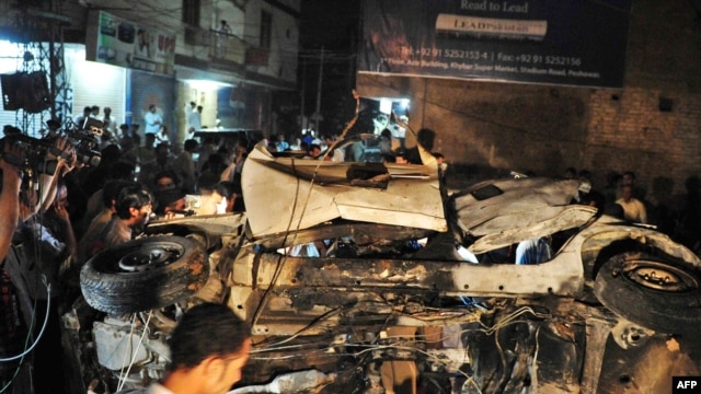 People gather around the destroyed car after the bomb explosion in Peshawar, which killed Nasrullah Afridi.