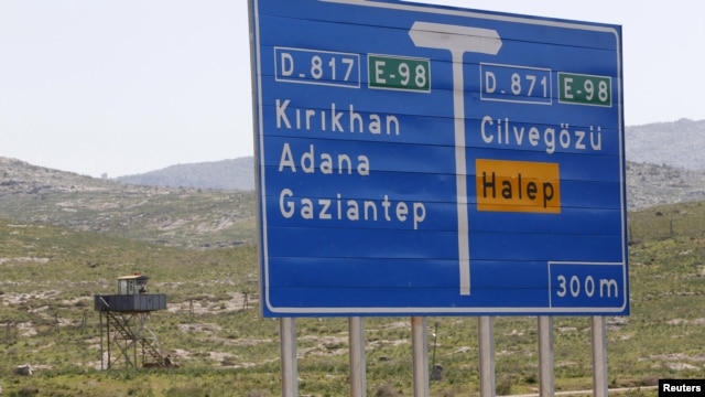 A Turkish soldier stands in a watchtower near a road sign showing directions to Cilvegozu border crossing and the Syrian city of Aleppo.