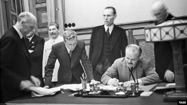 Soviet Foreign Minister Vyacheslav Molotov signs the nonaggression pact between Germany and the Soviet Union in Moscow on August 23, 1939, as Soviet dictator Josef Stalin looks on (left rear).