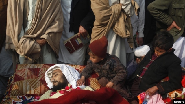 Children sit beside the body of one of the victims during a protest in front of the government offices in Peshawar.