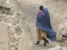 Afghanistan - A burqa-clad woman carries her child as she walks home through the ruins of war torn Kabul, 07Mar2008