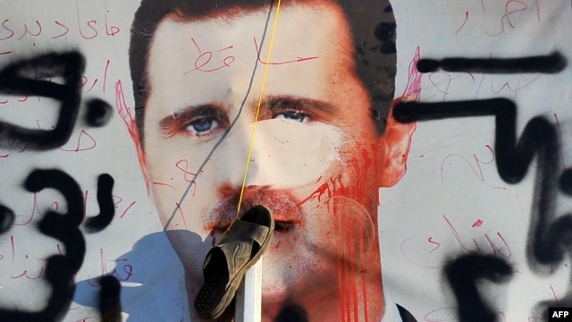 A sandal hangs on a vandalised poster of Syrian President Bashar al-Assad lying in a trash container in the northern city of Aleppo.