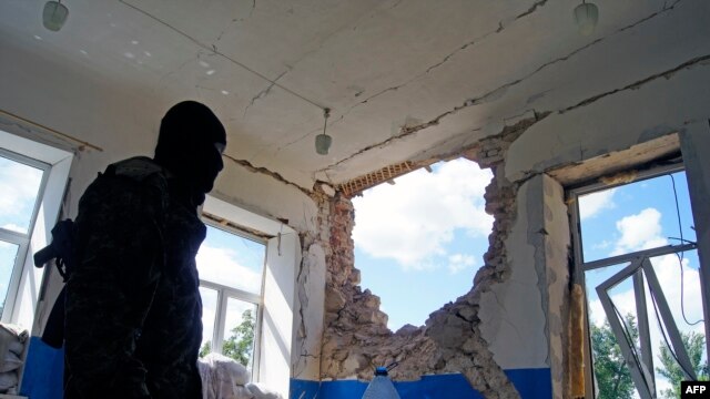 В Славянске вооруженный про-российский активист показывает журналистам повреждения, якобы нанесенные жилому дому в результате обстрела со стороны украинской армии