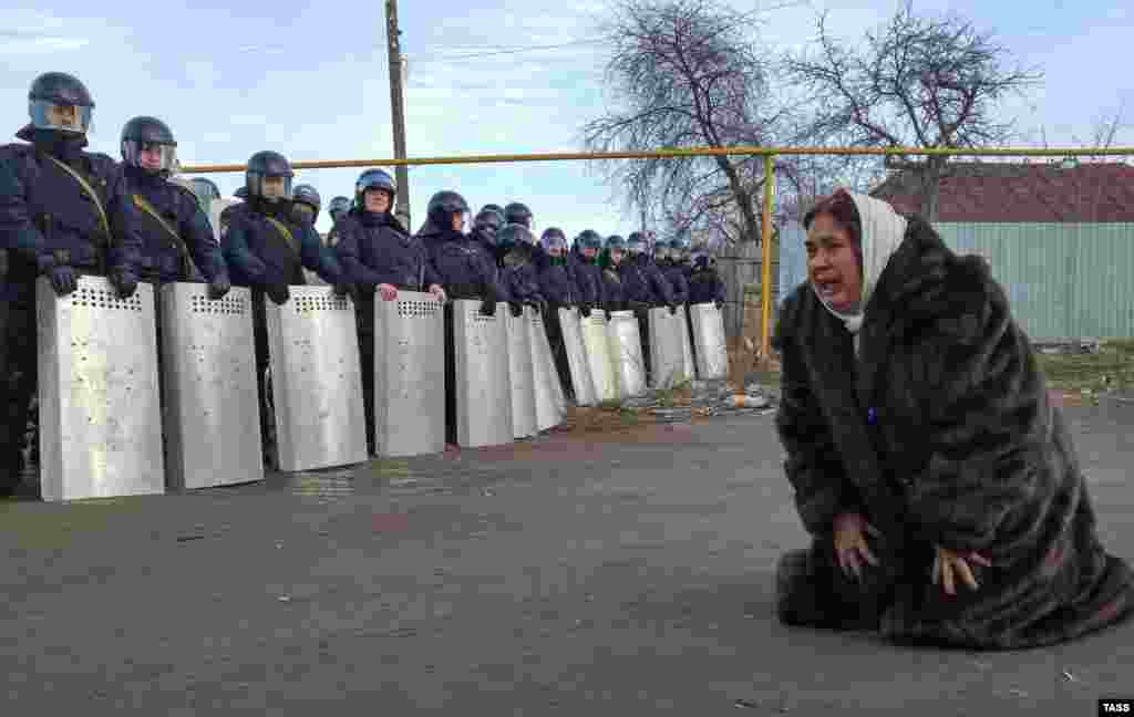 A Romany woman kneels and cries as riot policemen stand in a formation during a protest in the town of Plekhanovo, in the western Russian region of Tula, on March 17. (TASS/Sergei Starikov)