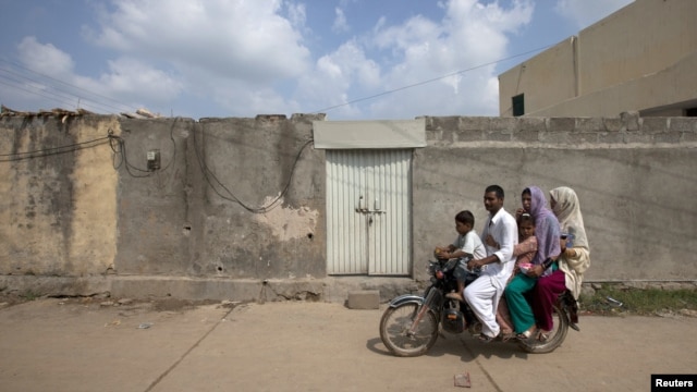 A family rides past the locked house of a Christian girl accused of blasphemy, on the outskirts of Islamabad.