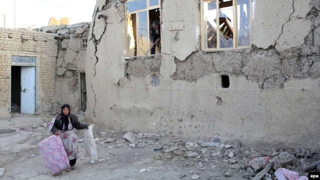 A woman carries a few belongings as she walks next to a severely damaged house in the city of Varzeqan, in the northwestern province of East Azerbaijan, on August 13.
