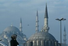 Turkey -- A woman waits for a bus next to a mosque in downtown Istanbul, 25Nov2006