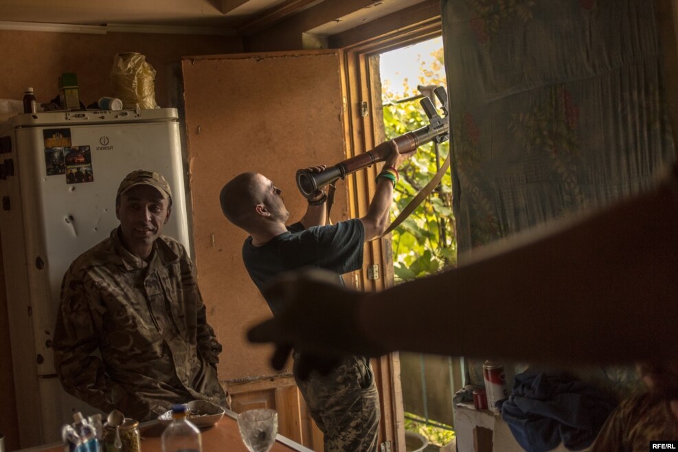 Little One inspects his weapon during the quiet of the daytime. Avram stands to his left.
