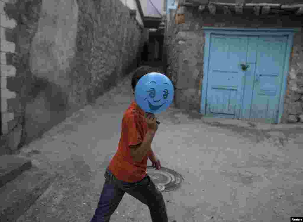 A boy hides his face behind a balloon on a street in Gimry.