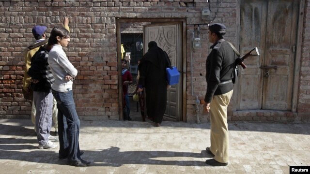 A policeman stands guard as female polio workers wait to administer polio vaccines to children in Lahore, Pakistan, on December 20.
