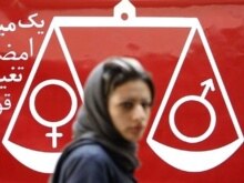 Iran -- An Iranian woman walks past a banner reading 
