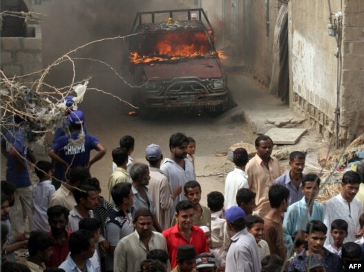 Onlookers gather near a burning vehicle in a troubled area of Karachi