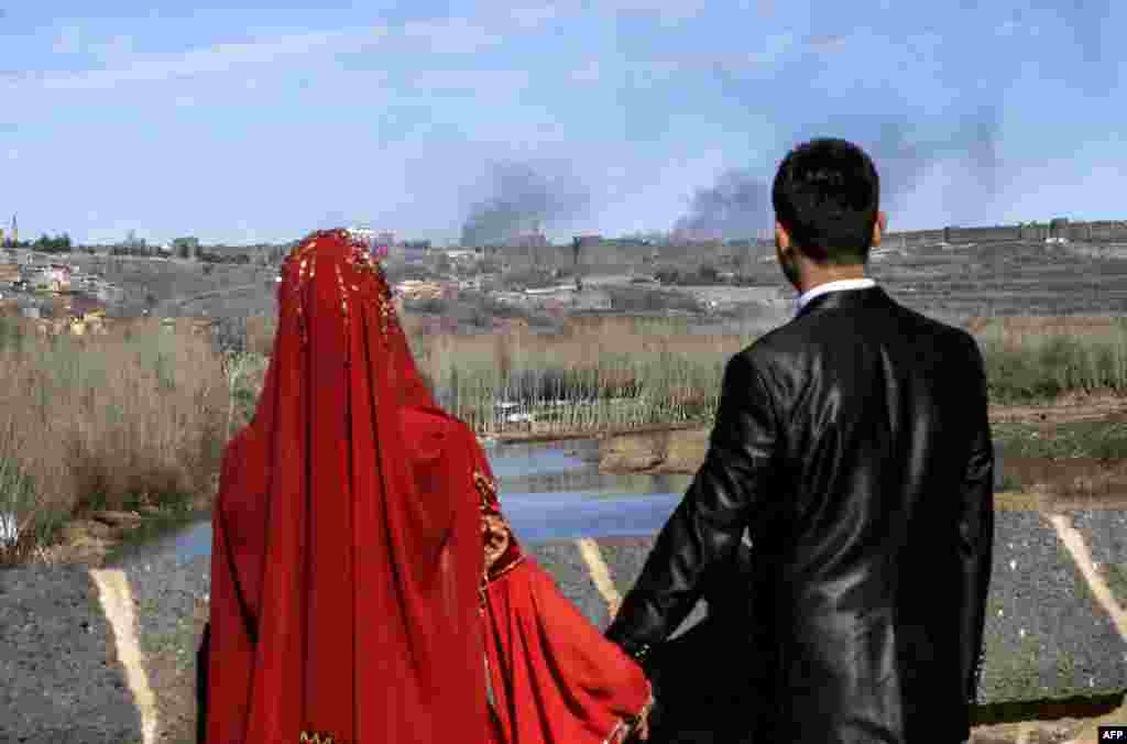 A couple holds hands for a wedding photo as they look at smoke rising over the district of Sur in Diyarbakir, Turkey, after clashes between Kurdish rebels and Turkish forces. (AFP/Ilyas Akengin)