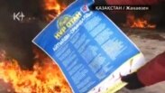 Жұмысшы киімін киген адам «Нұр Отан» партиясының плакатын отқа тастап жатыр. Жаңаөзен, 16 желтоқсан, 2011 жыл. (К-плюс телеарнасы бейнехабарынан алынған скриншот).