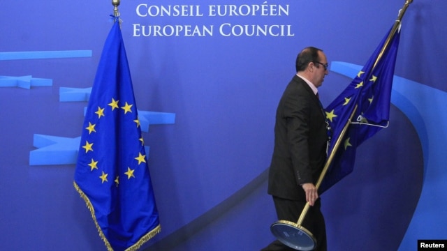 An employee at the EU council in Brussels on November 22 adjusts European Union flags at the entrance of the council headquarters for an EU leaders' summit discussing the bloc's long-term budget.
