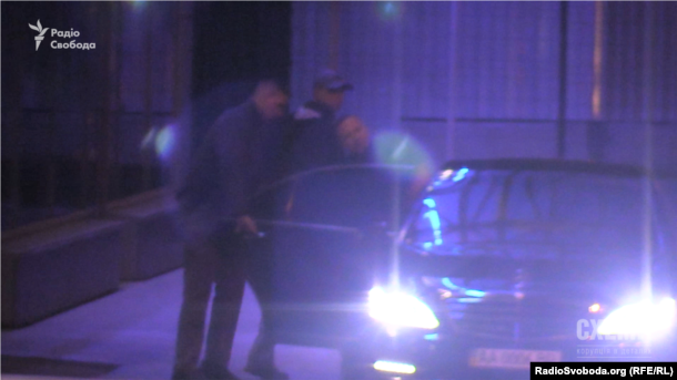 Охранник, который угрожал оружием журналистам, открывает двери авто российскому бизнесмену Павлу Фуксу