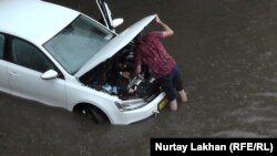 Водитель пытается завести машину, заглохшую из-за затопления улицы. Алматы, 17 июня 2016 года.