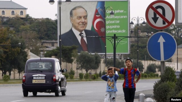 Azerbaijan -- Children wait for a bus in front of a billboard displaying a portrait of late President Heydar Aliyev, in Baku, 08Sep2012