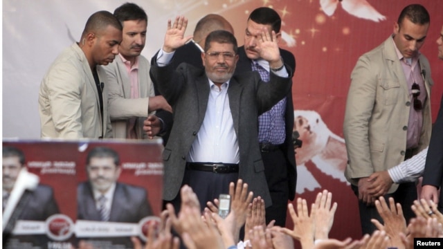 Egyptian President Muhammad Morsi (center) waves after speaking to supporters in front of the presidential palace in Cairo on November 23. 