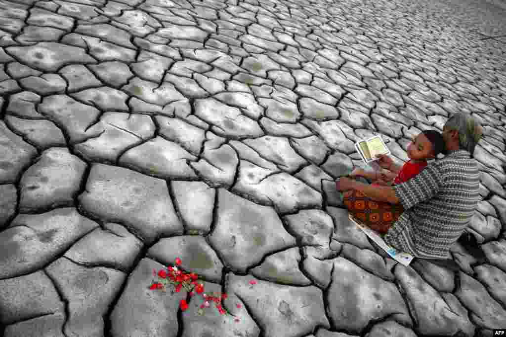 An Indonesian man and his son pray after offering flowers on dried volcanic mud for family members who died during a volcanic eruption in eastern Java island, as Indonesians mark Eid al-Fitr. (AFP/M. Andika)