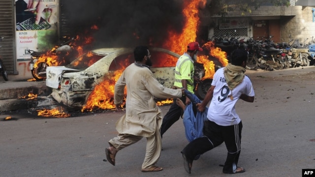 Pakistani volunteers and locals carry the dead body of a protester past a burning car after gunmen opened fire on a rally in Karachi on May 22.