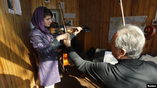 A teacher adjusts a student's violin work at the Kabul Music Academy.