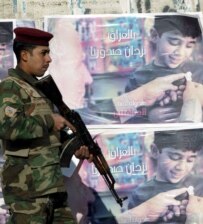 Iraqi soldier stands next to posters promoting reconciliation reading, 'By Iraq our chest will be adorned' in Baghdad on December 15 (epa)